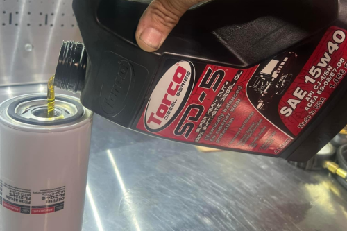 Expert Vehicle Oil Maintenance Tips | Domestic Diesel Chino, CA. Close-up photo capturing the skilled hands of a mechanic transferring torco oil into a can during an oil change service at shop