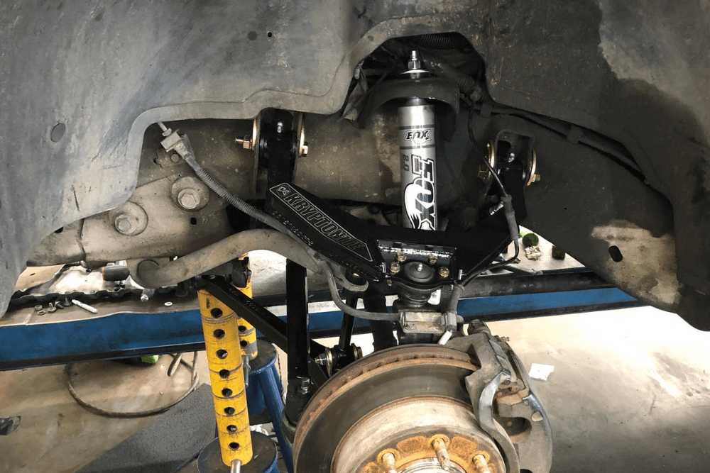 Front suspension repair in progress on a lifted truck, featuring a FOX shock absorber and Kryptonite upper control arm. The brake rotor and hub assembly are exposed during the upgrade. diesel truck repair in Chino, CA at Domestic Diesel & Auto Service.